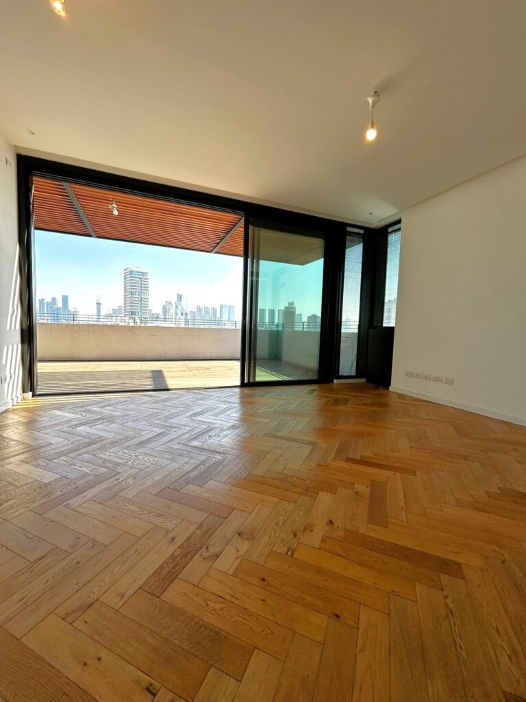 Bright and spacious living room in a Tel Aviv penthouse, with floor-to-ceiling windows and balcony access.