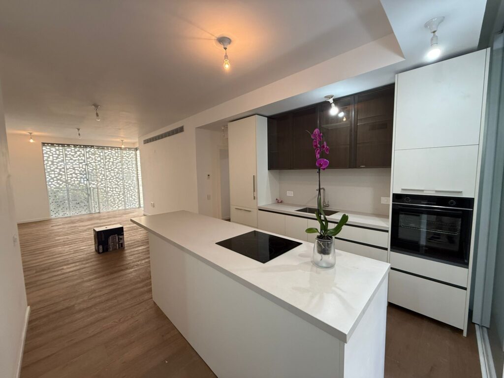 Modern open-plan kitchen with white island and wooden floors in Tel Aviv apartment