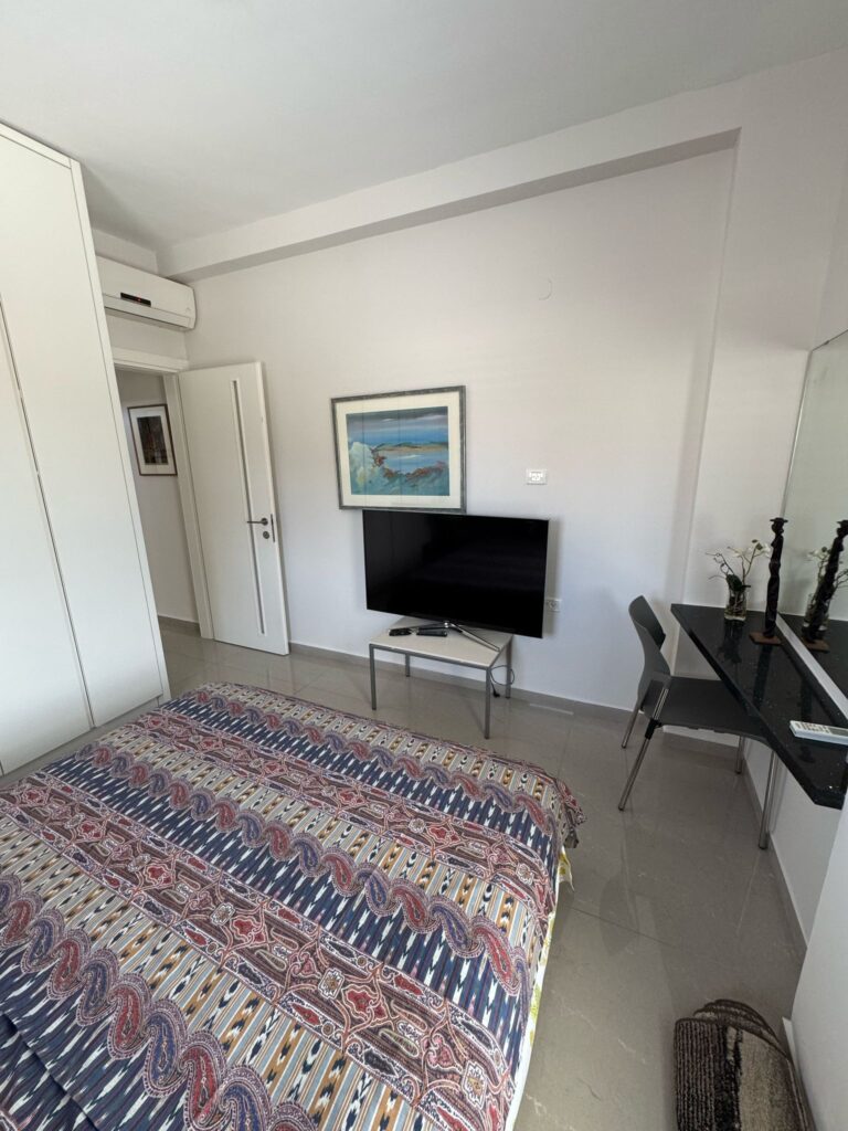 Bedroom with TV, modern décor, and large window in Tel Aviv apartment