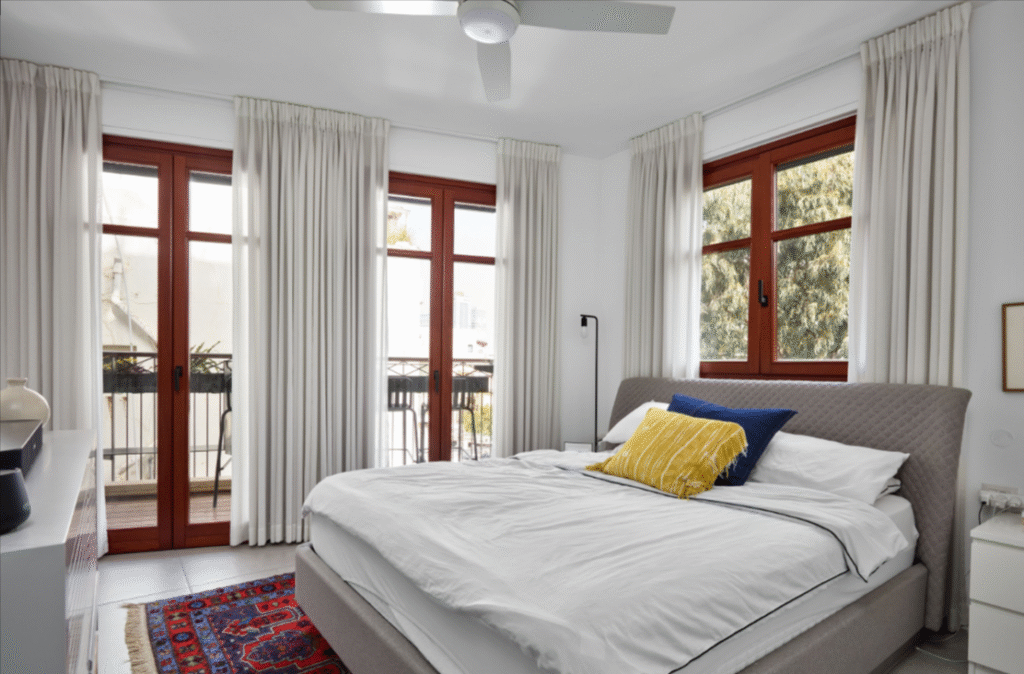 Sunlit bedroom with large windows and balcony access in Tel Aviv