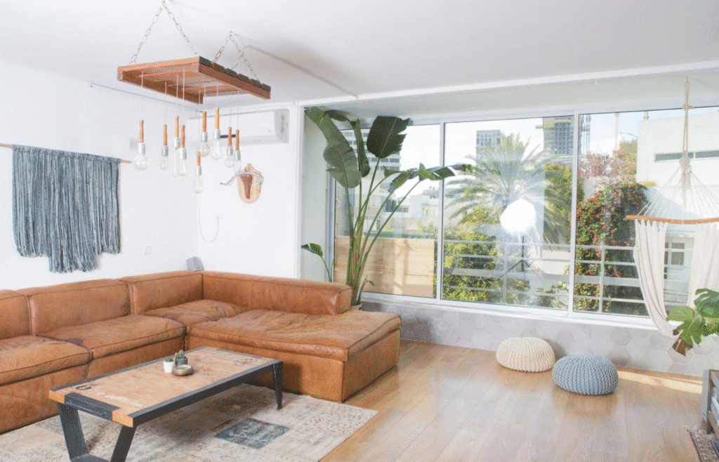 Sunlit living room with leather sofa and large windows in corner Tel Aviv apartment
