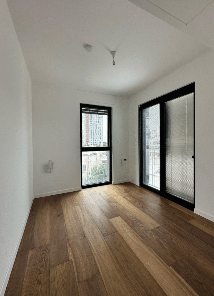 Sunlit bedroom with wooden floors and large windows in Tel Aviv