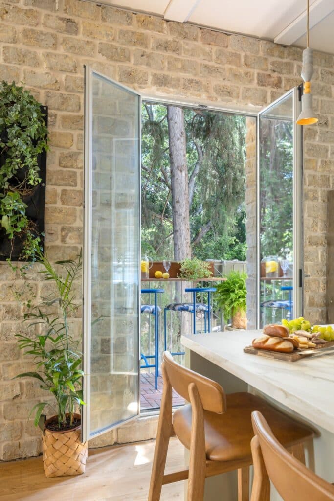 Open door to balcony from kitchen, surrounded by exposed brick and plants